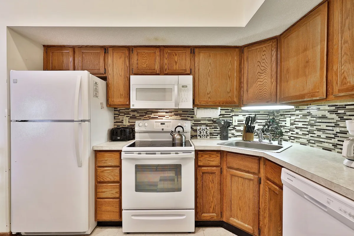 A full kitchen featuring a white refrigerator, stainless steel appliances, wooden cabinetry, and a textured backsplash. The counters are clear, inviting meal preparation and group activities. The space feels both practical and cozy, with enough room for prepping snacks or cooking a large meal.
