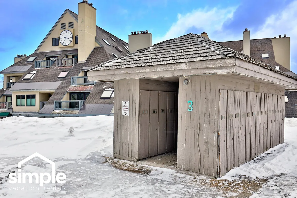 An exterior shot featuring lockers, a clock tower, and a snow-covered area where guests gather. This communal area ties into the exploration theme, hinting at nearby amenities like the Snowshed upper parking lot (where Tesla chargers are available) and the property's proximity to local activities.