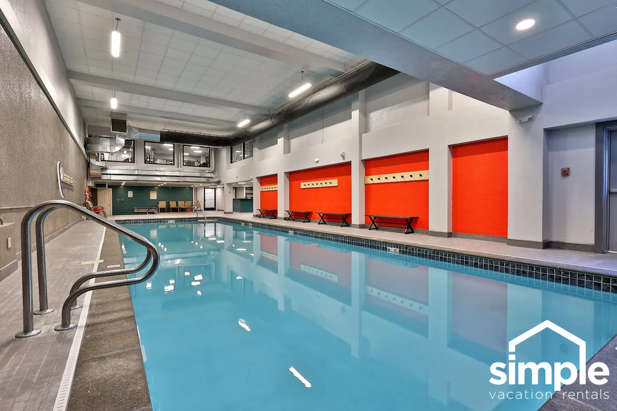 An inviting indoor swimming pool area with bright red accent walls and benches along the poolside, suggesting a lively and social atmosphere ideal for groups to unwind and socialize after skiing.