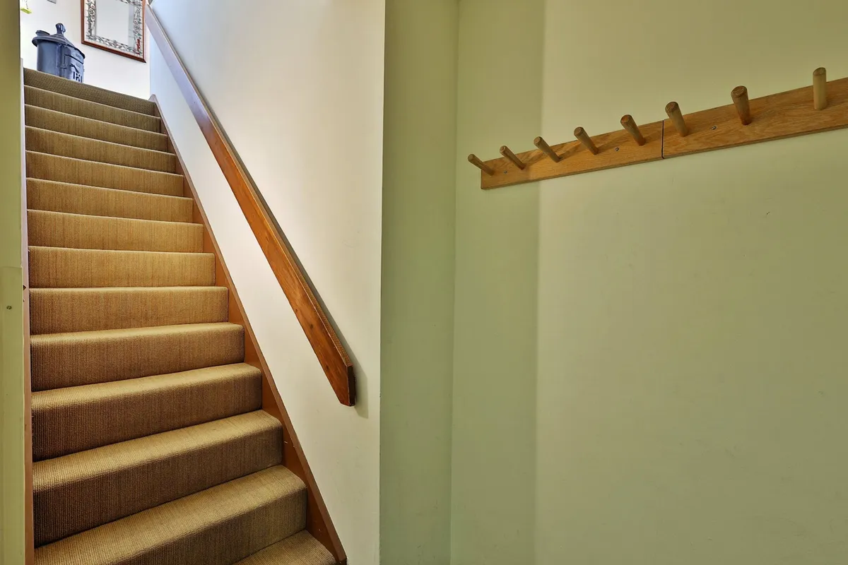 This image captures the staircase with a wooden handrail and a coat rack, suggesting the journey from the condo entrance up one flight of stairs, which directly relates to the accessibility note in the section. The cozy and welcoming mood introduces guests to the property and highlights the first impression upon arrival.
