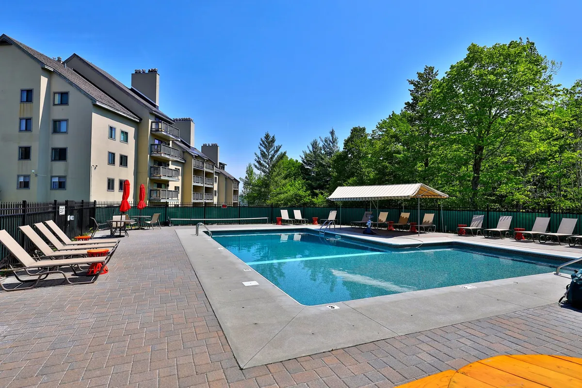 A spacious outdoor pool area featuring lounge chairs, surrounding trees, and a cabana, showcasing an ideal setting for summer fun, sunbathing, and group activities.