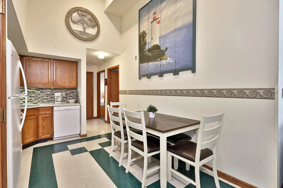 A bright dining area with a wooden dining table surrounded by chairs, set near large kitchen cabinetry and a wall painting. The space is bathed in natural light, creating a welcoming atmosphere that encourages group meals and conversation.