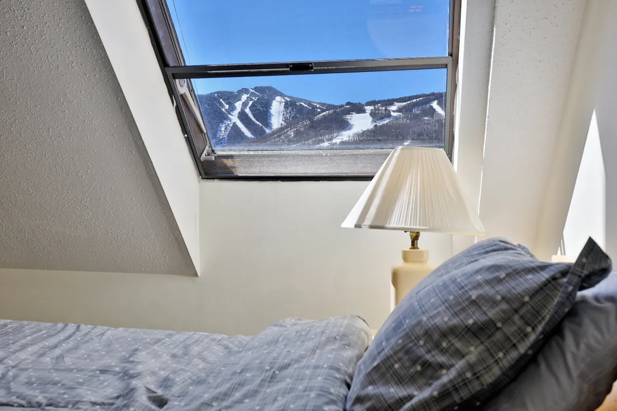 A serene bedroom with gray bedding, a softly lit bedside lamp, and a window offering breathtaking views of the mountains. The tranquil setting is perfect for unwinding after a day of adventure, with natural light pouring in to create a calm, romantic mood.