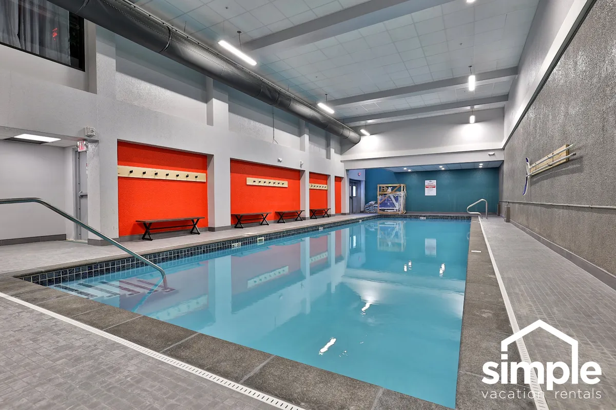 A vibrant indoor swimming pool area with colorful accent walls, benches along the poolside, and people enjoying the space. The atmosphere is cheerful, suggesting a great place to relax and unwind après-ski.
