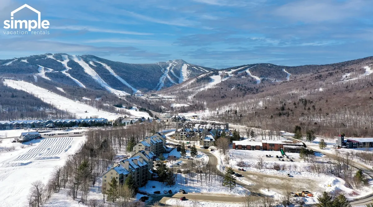 A scenic view of snow-covered mountains and ski slopes, with residential buildings and roadways in the foreground. The image evokes the excitement of winter sports and the proximity to the slopes, highlighting the adventurous mood of the destination.
